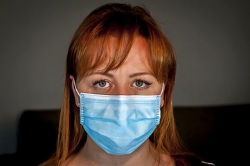 Attractive Caucasian young woman in a protective face mask looking in the eyes of the photographer. COVID 19 novel coronavirus disease outbreak concept image.