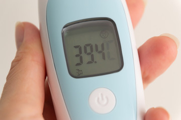 A hand holds a modern thermometer scanner displaying high temperature. Fever as a sign of coronavirus Covid-19 disease