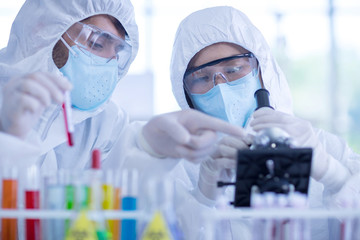 A female scientist wearing a mask and looking through the microscope in the laboratory, Concept, The scientists wear white protective clothing is experimenting with drug anti- Coronavirus, Covid19