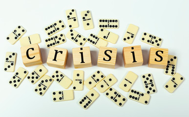 Around the wooden blocks that make up the word CRISIS, domino chips are scattered