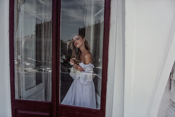 A charming beauty of the bride's Fashion pose at the window. Portrait of a modern bride through the window.