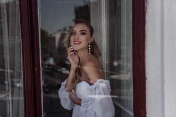 Fototapeta premium A charming beauty of the bride's Fashion pose at the window. Portrait of a modern bride through the window.