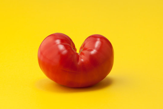 Heart shaped tomato on a yellow background. Funny, unnormal vegetable concept. Ugly organic vegetables. Horizontal orientation. Closeup. Copy space