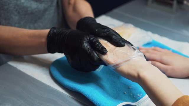 Spa Salon. Manicure. Paraffin Hand Bath. process paraffin treatment. Bowl, additive. Wax bathtub Care. Nail care. Nail artist doing manicure. Professional master putting mitten on hand customer