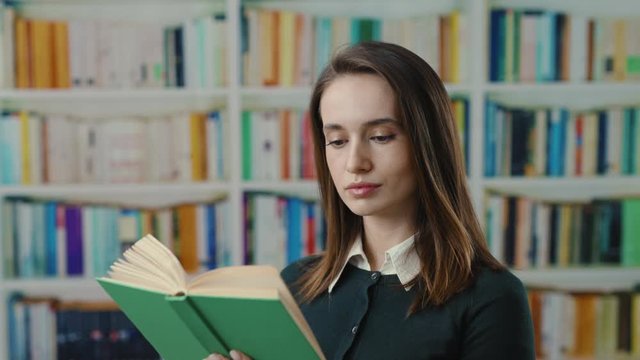 Young cheerful woman student college girl reading stor book literature for study smiling satisfied enjoying stay at contemporary library.