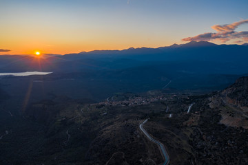 Aerial view of Delphi, Greece, the Gulf of Corinth, orange color of clouds, mountainside with layered hills beyond with rooftops in foreground