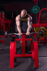 Powerful muscular man doing biceps exercise with barbell on the bench