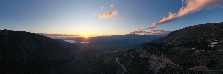 Aerial view of Delphi, Greece, the Gulf of Corinth, orange color of clouds, mountainside with layered hills beyond with rooftops in foreground