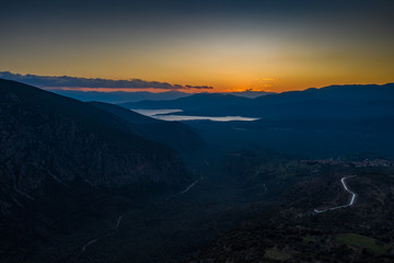 Aerial view of Delphi, Greece, the Gulf of Corinth, orange color of clouds, mountainside with layered hills beyond with rooftops in foreground