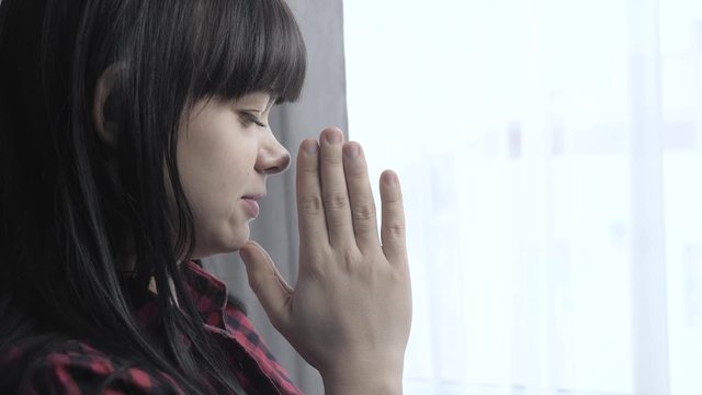 brunette girl makes a wish prayers bedtime religion concept. prayer woman mom lifestyle indoors praying by bed front of window