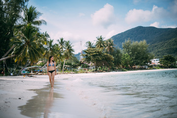 Beautiful woman in a swimsuit walks on a tropical beach