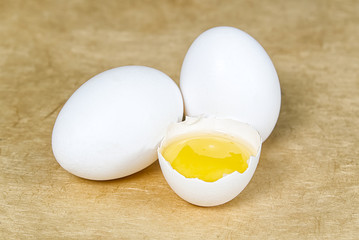 chicken white eggs with half broken egg on beige textured background