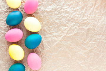 Rustic Easter frame border with colored eggs on crumpled craft paper. Pattern of pink, blue and yellow painted eggs. Minimal Easter concept. Flat lay, top view, copy space.