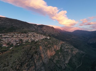 Aerial view of Delphi, Greece, the Gulf of Corinth, orange color of clouds, mountainside with layered hills beyond with rooftops in foreground