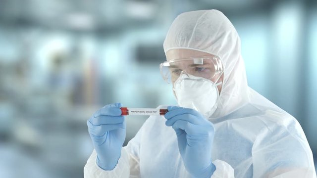 A laboratory assistant wearing protection gear examines vial with pneumococcal disease blood test