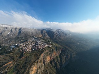 Aerial view of Delphi, Greece at sunrise, the Gulf of Corinth, Morning fog over mountains, hoarfrost on roofs, mountainside with layered hills beyond with rooftops in foreground