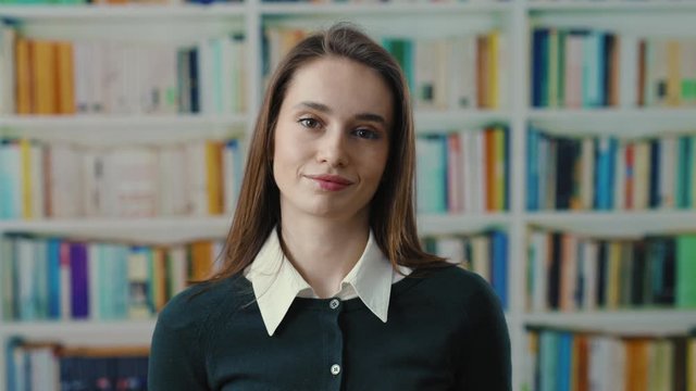 Uncertain woman young student doubting at camera cant help with situation shrugging her shouders near bookshelves. Library. Education and people concept.