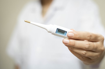 Woman hand holds analogue medical thermometer to  measure the body temperature, protection from virus, flu & respiratory diseases.
