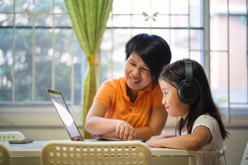 Asian girl and her teacher using laptop for online study during homeschooling at home....