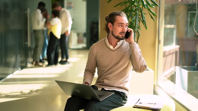 Smart casual Caucasian IT professional working with software update system on modern laptop computer using cellphone connection for talking and consultancy with partner, concept of entrepreneurship