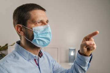 Side view portrait of adult caucasian man wearing protective medical mask on his face to protect from virus bacteria or pollution to prevent disease spread pointing finger indoor