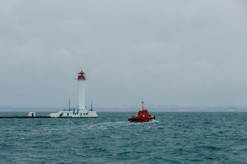 a small red tugboat swims past the lighthouse in the port