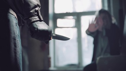 Back view of armed man, holding the knife in his hands. Scared young woman standing in the background in front of the killer. Concept of violence, murder