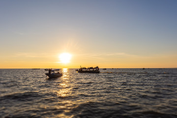Fototapeta premium Sunset at Tonle Sap Lake, Cambodia, near the Kampong Phluk Floating Village and Siem Reap. Tourism boats cruising on the water to enjoy the breathtaking colorful sunset. Sunset horizon over the sea.