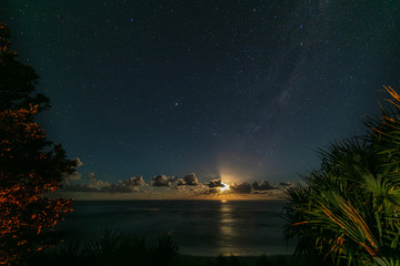 Moon rise at the beach of village of Yeppoon, Queensland, Australia. At the shore of the pacific ocean near Sunshine Coast. Moon rising in between the clouds and reflecting in the water of the sea.  