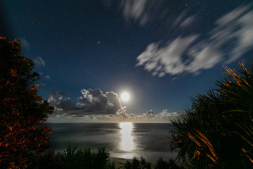 Moon rise at the beach of village of Yeppoon, Queensland, Australia. At the shore of the pacific ocean near Sunshine Coast. Moon rising in between the clouds and reflecting in the water of the sea.  