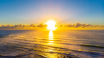 Sun rise at the beach of village of Yeppoon, Queensland, Australia. At the shore of the pacific ocean near Sunshine Coast. Sun rising in between the clouds and reflecting in the water of the sea.  