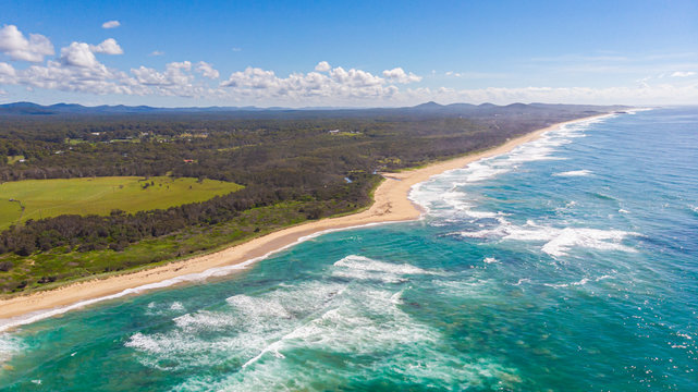 Aerial view of the shoreline of Sunshine Coast, Queensland, Australia. Drone view over the beaches of the Australian pacific coast. Waves crashing in the rocks of the sea. Small clouds on the blue sky