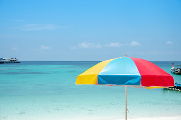 Beautiful multi colour or rainbow beach umbrella with beautiful blue ocean and blue sky background