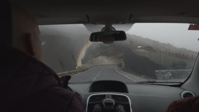 A slowmotion view from a windshield of a car that is driving past the dark volcanic rocks covered in black ashes. Everything around is misty because of the steam and the background can't be seen