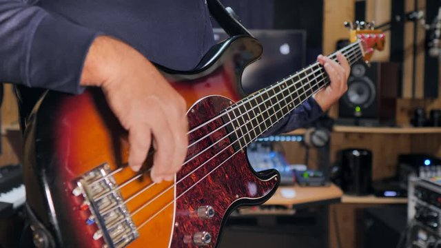 A bass player playing his electric bass guitar in a home recording studio. Static shot