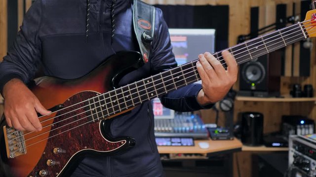 A bass player playing his electric bass guitar  in a home recording studio. Static shot