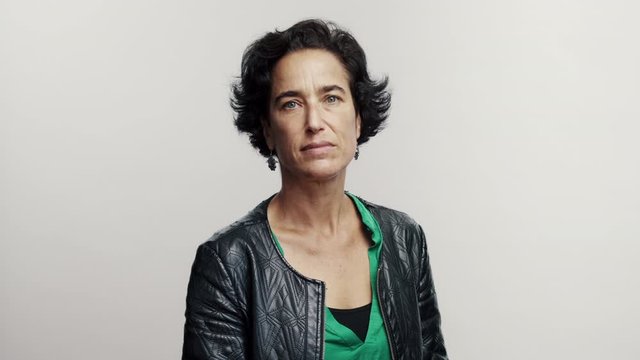 Mature woman with short hair looking at camera folding hands and smiling.  Middle aged woman on white background.