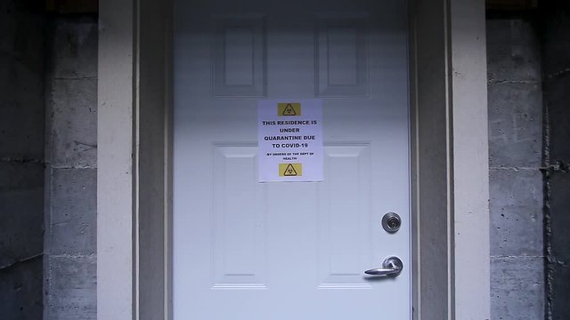 A man closes a door with a self isolating residence with a quarantine sign on the front warning of the Covid-19 virus. HD 24FPS.