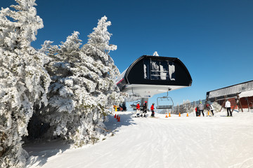 skiers on slope and ski lift with snow covered trees chairlift at background