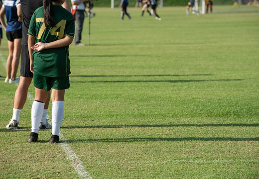 Substitute football player standing near her coach on a sideline, ready to get in a pitch for playing time in a girl youth soccer tournament. 