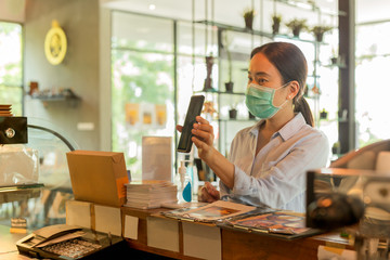 Woman customer with protective mask paying bill by cell phone in cafe.