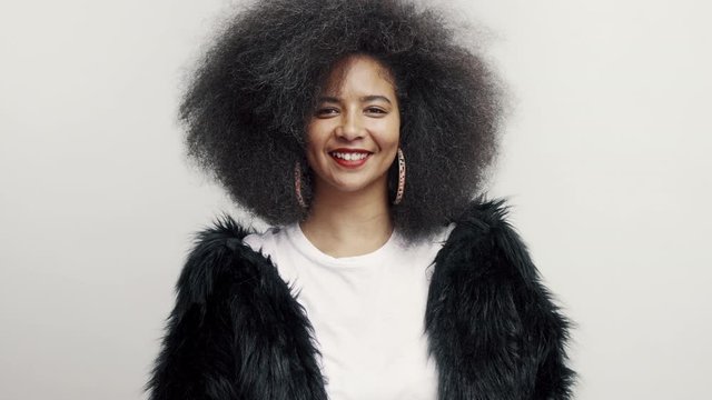 Close up of a happy african american woman. Woman in afro hairstyle wearing fur coat smiling on white background. 