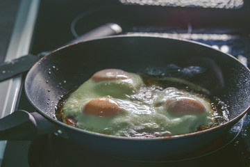 Close up on frying pan frying three organic eggs in oil or lard on the glass cooktop range stove in dark kitchen back illuminated sunny side up eggs