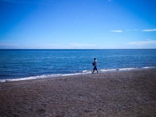 Tropical Beach Scenery With A Man Walking Fishing By The Beach In The Clear Sunny Blue Sky At The Village, Umeanyar, North Bali, Indonesia