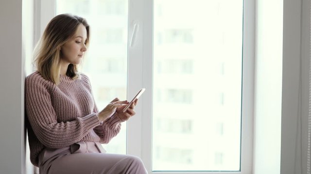Woman blogger browsing phone sitting on window. Concept of modern work and popularity in social media. Human using the smartphone