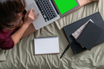 Young woman drinking coffee in her bed and checking her laptop, top view