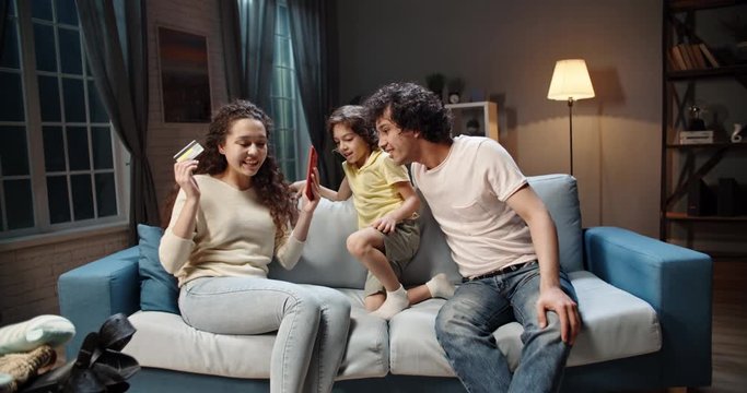 Asian family buys tickets for cheap flights on smartphone with credit card then funnily celebrates their upcoming adventure - happy family, travelling concept 4k footage