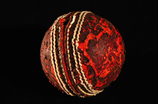A close up view of an old, well used red cricket ball on black background