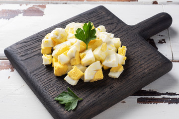 Boiled chicken egg finely chopped on a wooden Board with parsley leaves.
