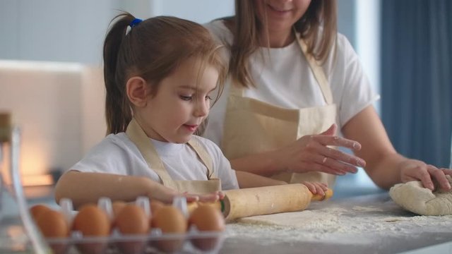 Mom helping daughter to roll out dough. Mom and little daughter roll out the dough for making cookies. using rolling pin and making biscuits.